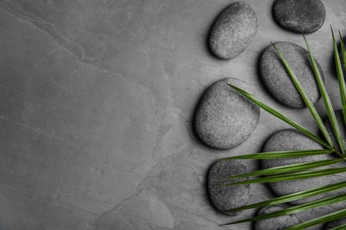 Photo of Zen stones and tropical leaf on dark background, top view with space for text