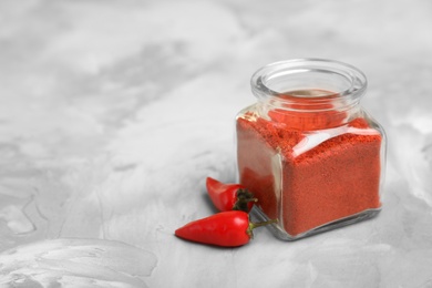 Photo of Jar of chili pepper powder and fresh vegetable on table. Space for text