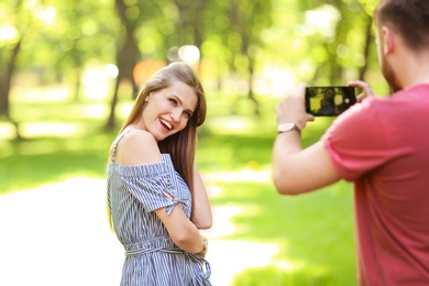 Photo of Young man taking photo of beautiful woman in green park on sunny spring day