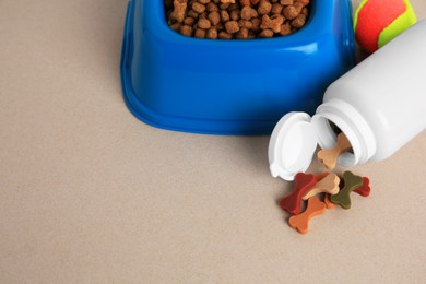 Photo of Bottle with vitamins, toy and dry pet food in bowl on beige background, space for text