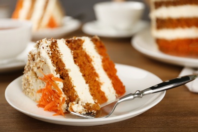 Plate with piece of tasty carrot cake and fork on wooden table, space for text