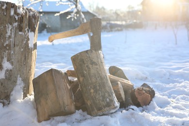 Photo of Metal axe in wooden log and pile of wood outdoors on sunny winter day