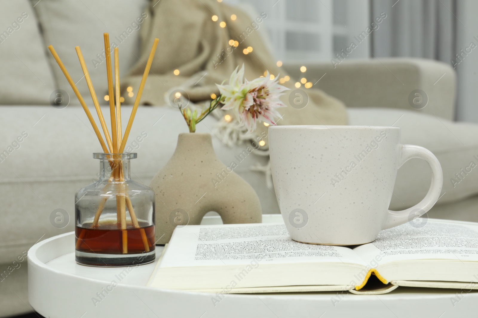 Photo of Cup of drink, air freshener and book on coffee table indoors