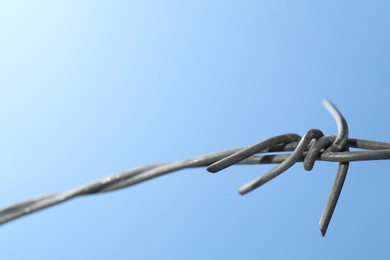 Photo of Metal barbed wire on light blue background, closeup