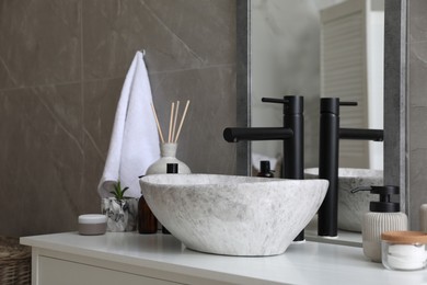 Photo of Stone vessel sink with faucet and toiletries on white countertop in bathroom