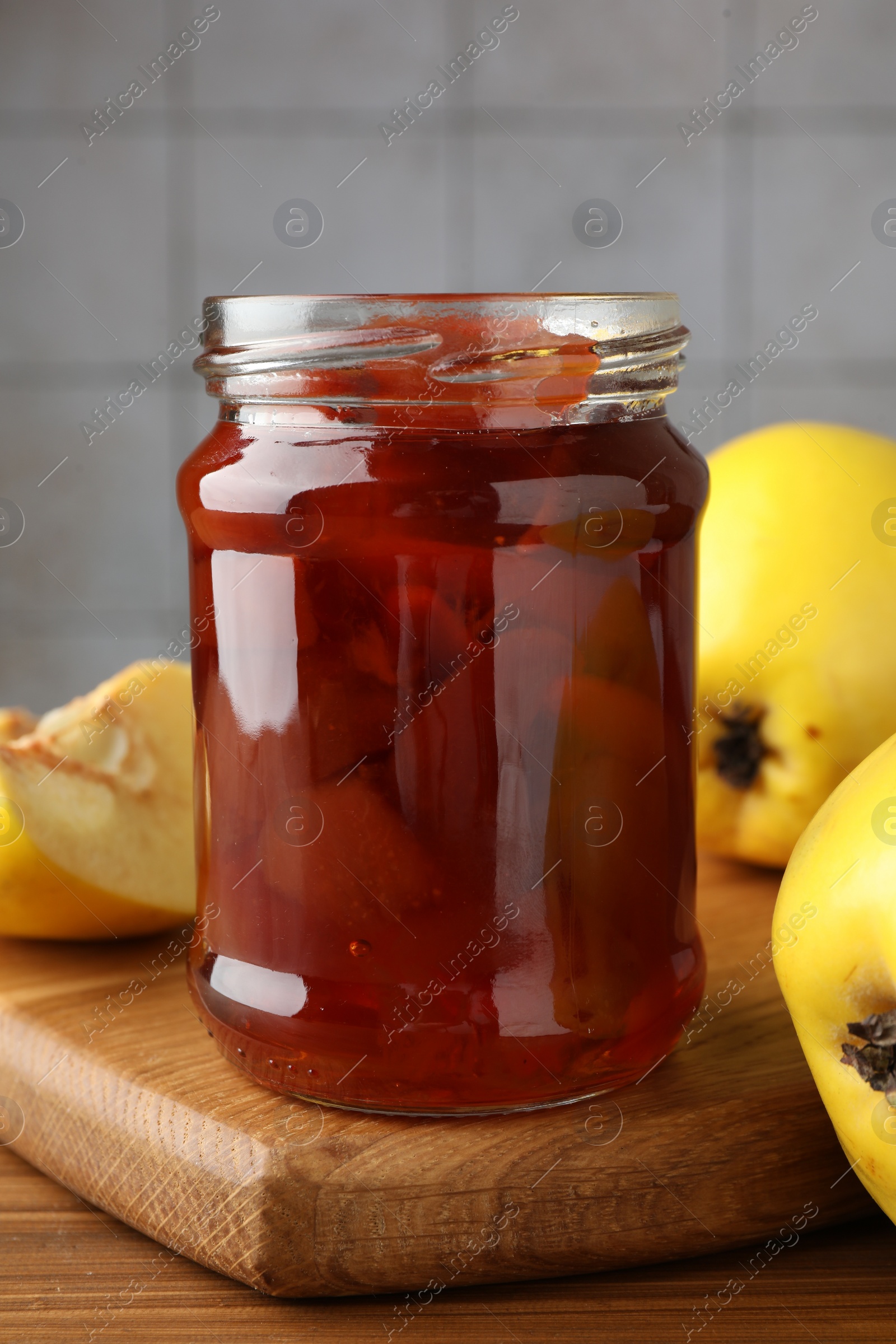 Photo of Tasty homemade quince jam in jar and fruits on wooden table, closeup