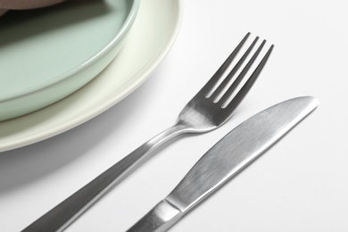 Photo of Fork, knife and plates on white table, closeup