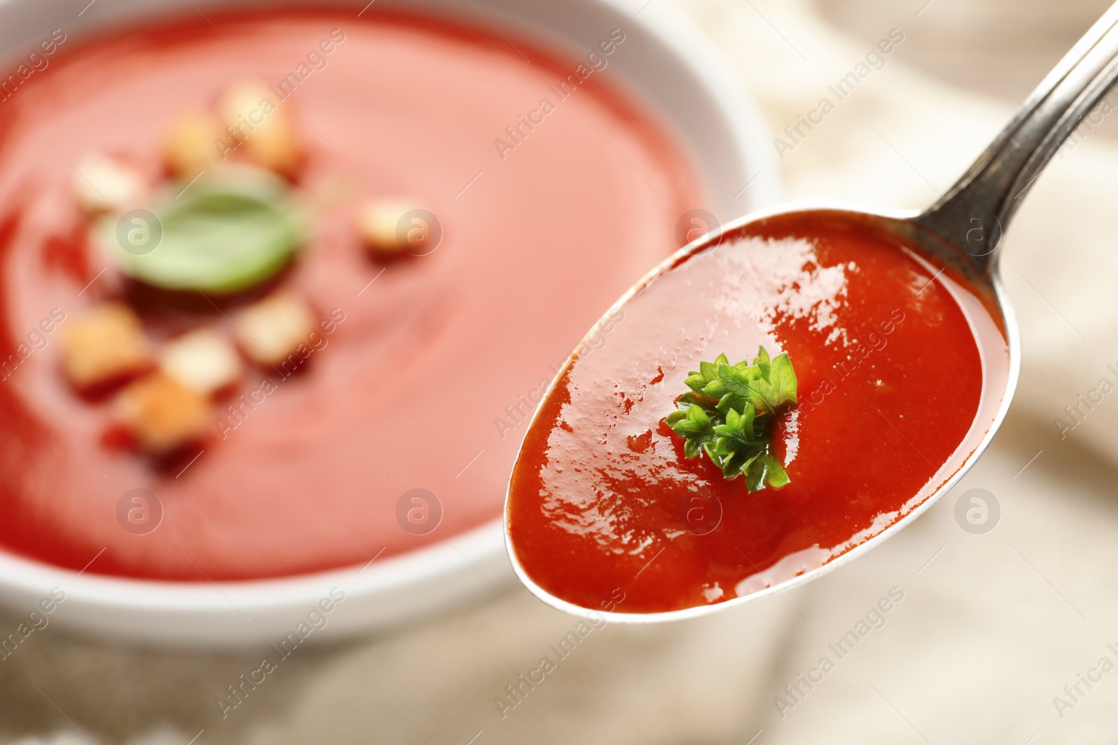 Photo of Spoon with fresh homemade tomato soup on blurred background, closeup. Space for text