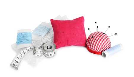 Photo of Pincushions, sewing pins, threads, cloth and measuring tape isolated on white
