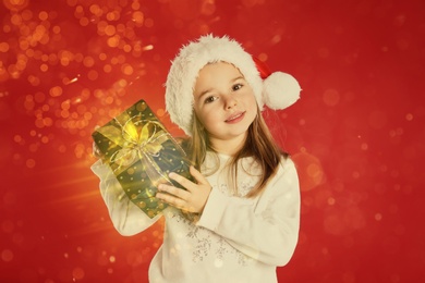 Cute child in Santa hat with Christmas gift on red background