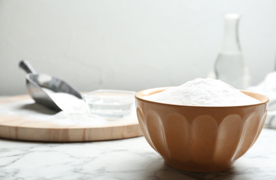 Photo of Baking soda in bowl on white marble table. Space for text