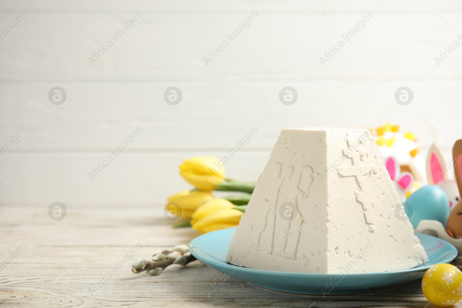 Photo of Traditional cottage cheese Easter paskha and dyed eggs on white wooden table, space for text