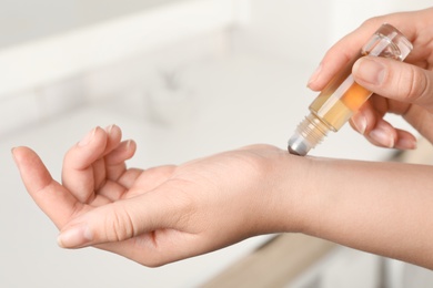 Photo of Woman applying essential oil on wrist indoors, closeup