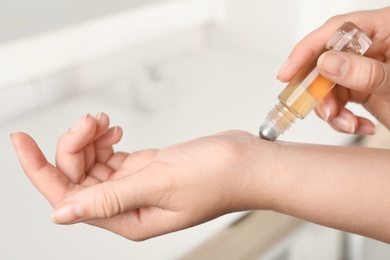 Woman applying essential oil on wrist indoors, closeup