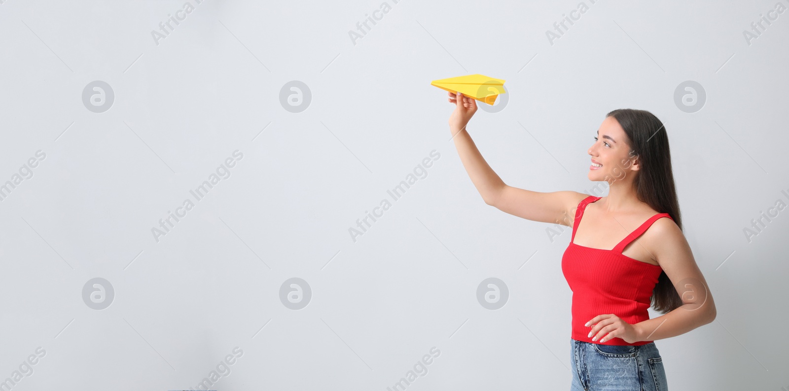 Photo of Beautiful young woman playing with paper plane on light grey background. Space for text