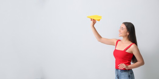 Photo of Beautiful young woman playing with paper plane on light grey background. Space for text