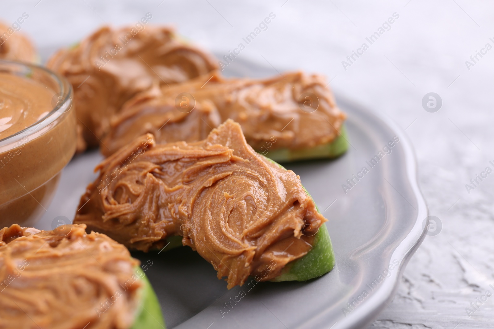 Photo of Slices of fresh green apple with peanut butter on light textured table, closeup. Space for text