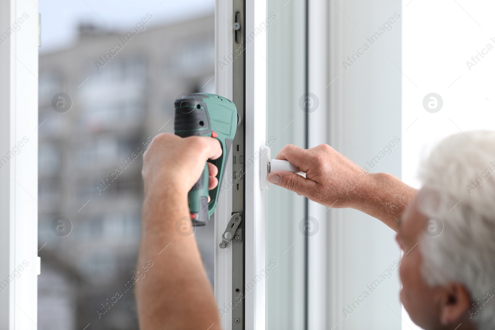 Photo of Construction worker repairing plastic window with electric screwdriver indoors, closeup