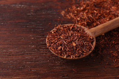 Photo of Spoon with dry rooibos leaves on wooden table, closeup. Space for text