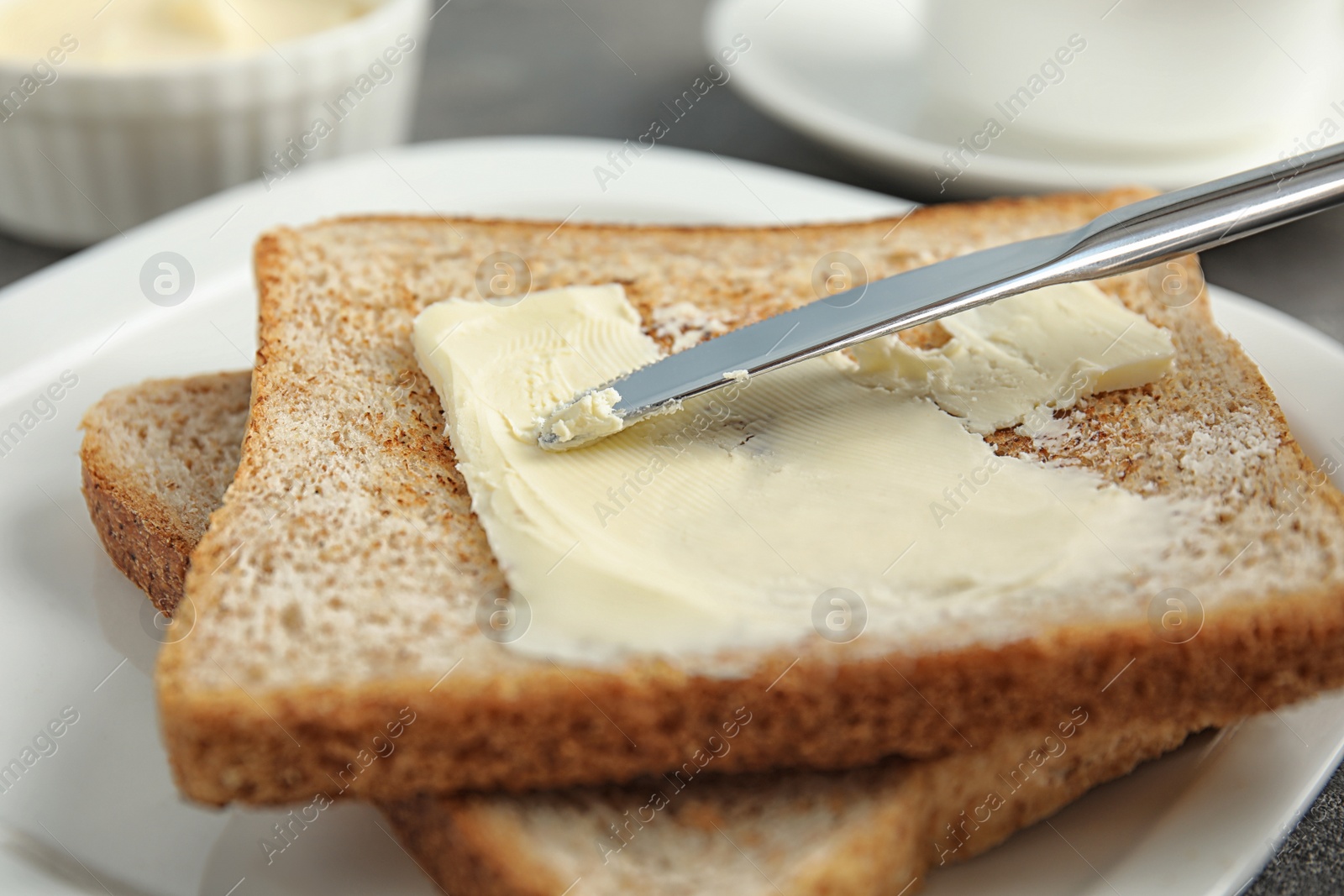 Photo of Spreading tasty butter onto slice of bread with knife on plate, closeup