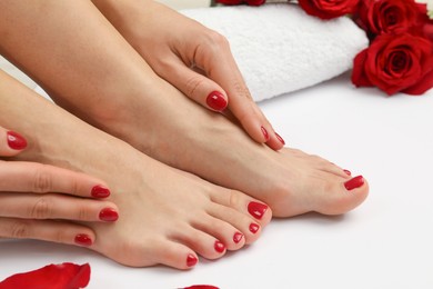 Photo of Woman with stylish red toenails after pedicure procedure and rose petals on white background, closeup