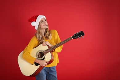 Photo of Young woman in Santa hat acoustic guitar on red background, space for text. Christmas music