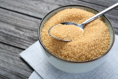 Photo of Brown sugar in bowl and spoon on black wooden table, closeup