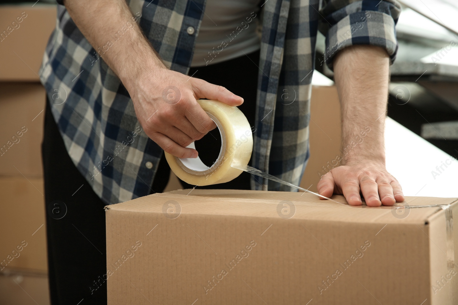 Photo of Man taping cardboard box indoors, closeup view