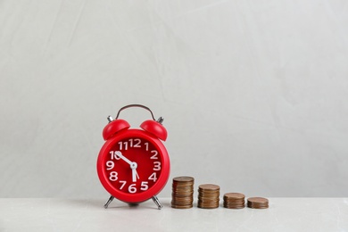 Photo of Red alarm clock and stacked coins on light grey marble table. Money savings