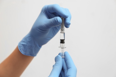 Doctor holding syringe with COVID-19 vaccine on light background, closeup