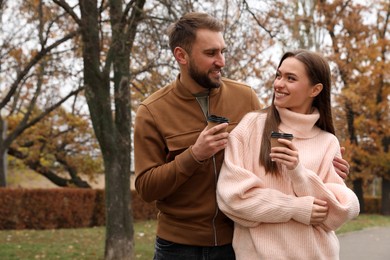 Photo of Happy couple wearing stylish clothes with cups of coffee in autumn park