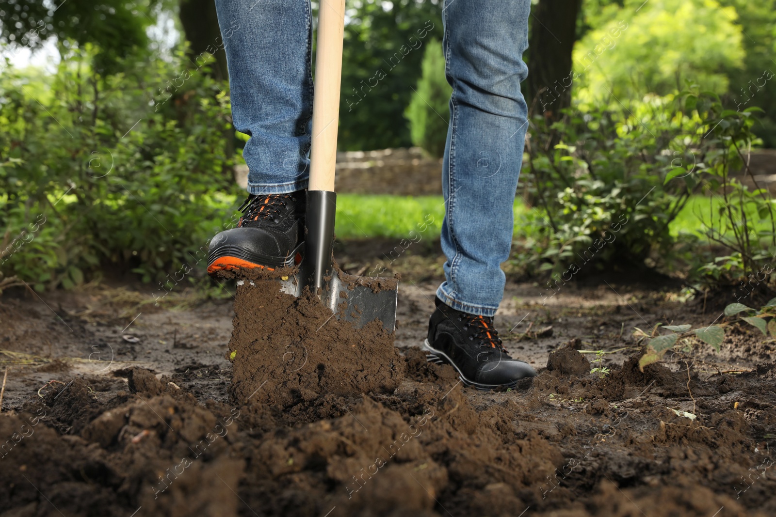 Photo of Worker digging soil with shovel outdoors, closeup