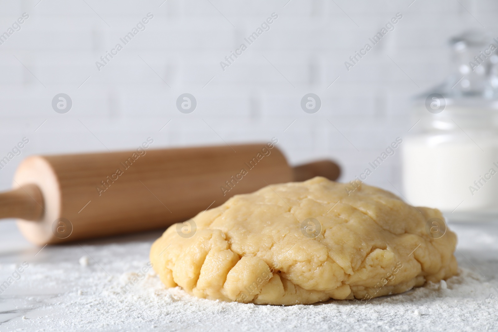 Photo of Making shortcrust pastry. Raw dough, flour and rolling pin on table