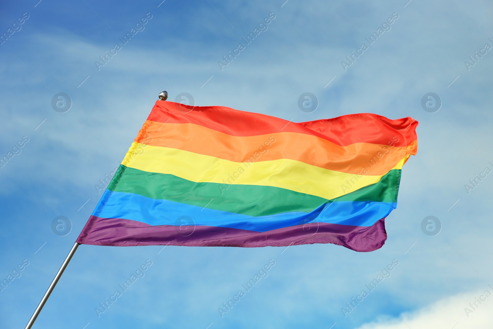 Photo of Bright rainbow gay flag fluttering against blue sky. LGBT community