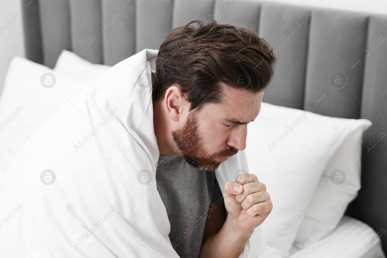 Photo of Sick man coughing on bed. Cold symptoms