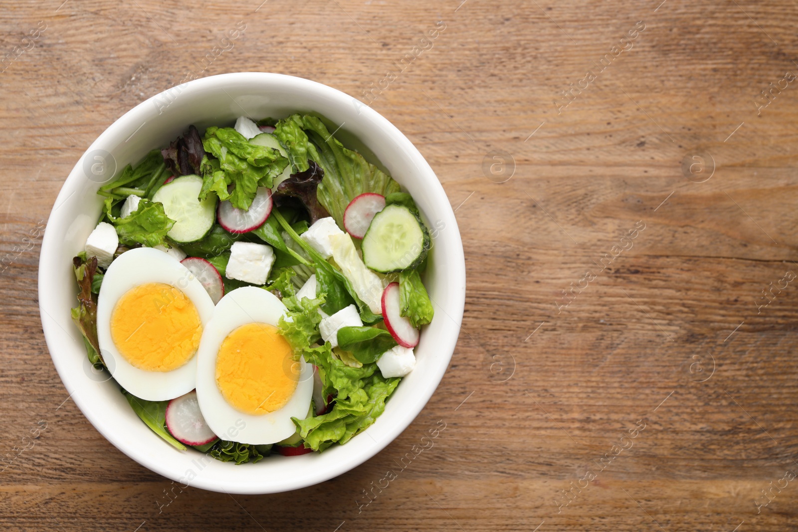 Photo of Delicious salad with boiled egg, feta cheese and vegetables on wooden table, top view