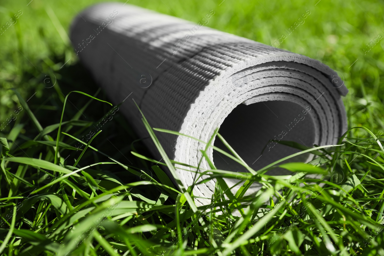 Photo of Rolled karemat or fitness mat on green grass outdoors, closeup. Space for text