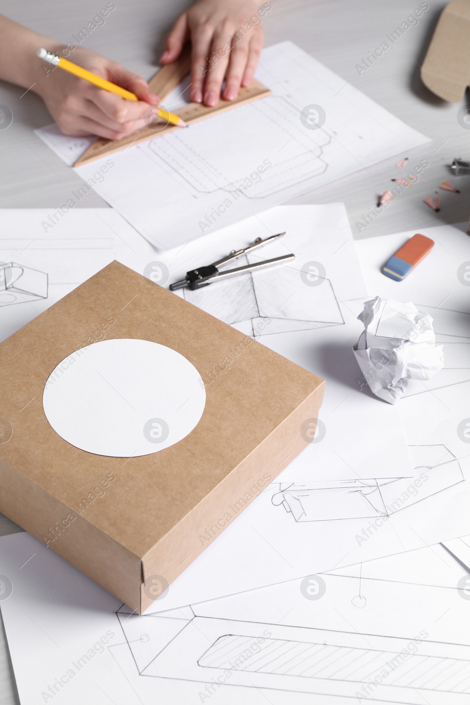 Photo of Box and stationery on drawings, closeup. Woman creating packaging design at wooden table, selective focus