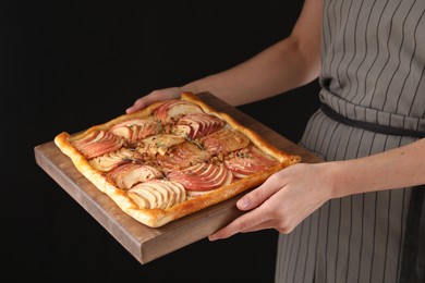 Woman holding freshly baked apple pie with nuts on black background, closeup