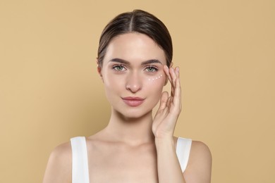 Photo of Young woman with cream around eye on beige background