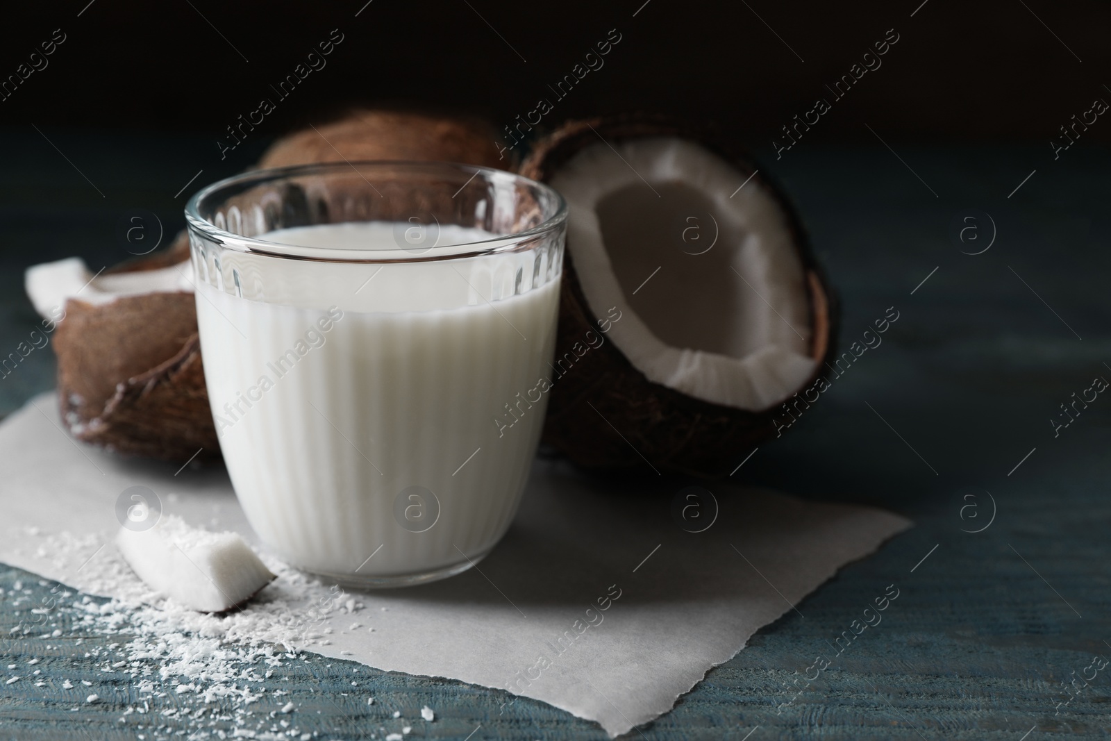 Photo of Glass of delicious coconut milk, flakes and nuts on wooden table, space for text