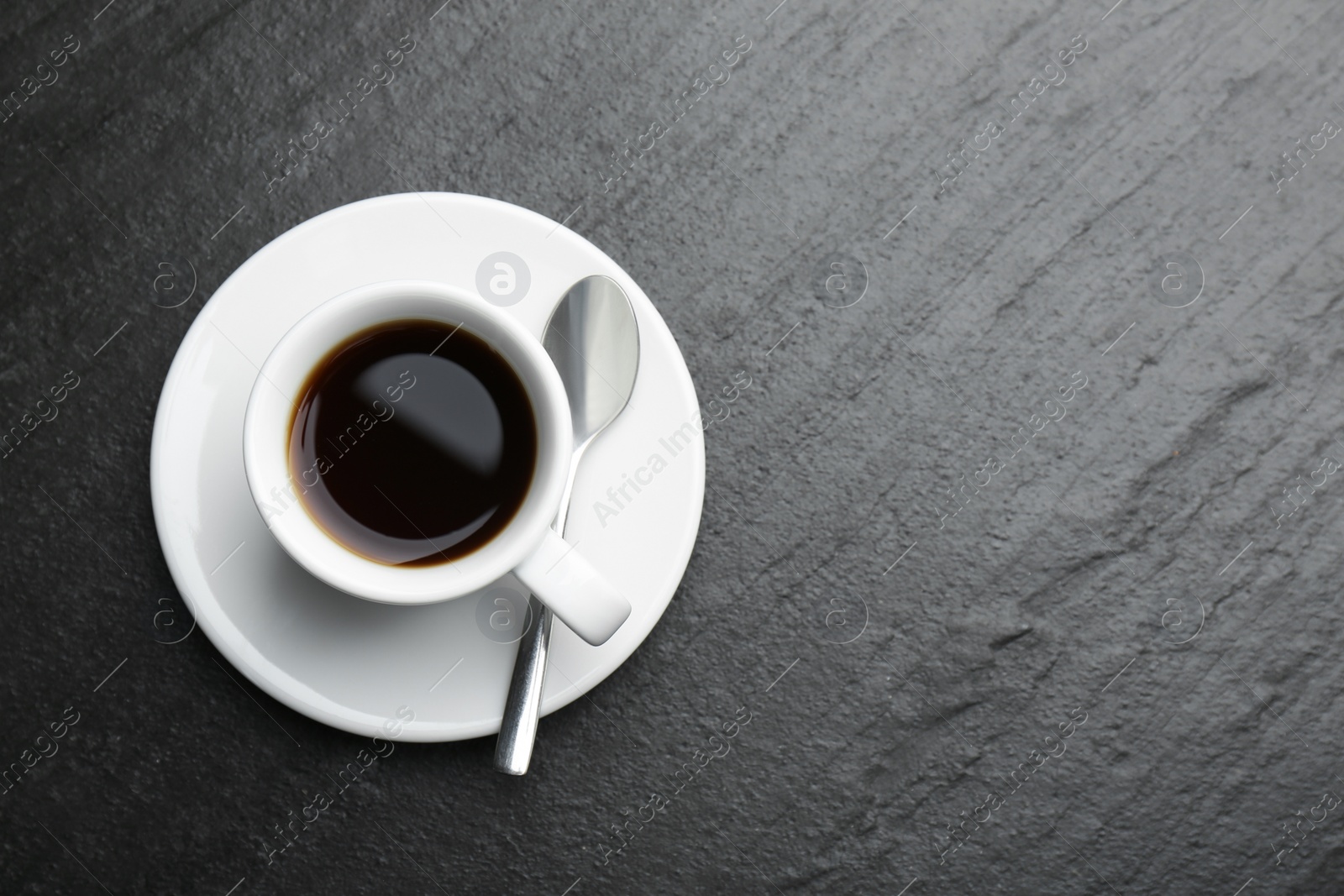 Photo of Hot coffee in cup, spoon and saucer on dark textured table, top view. Space for text