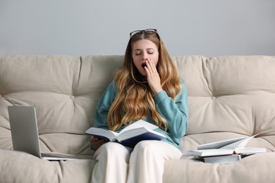 Young tired woman studying on couch indoors