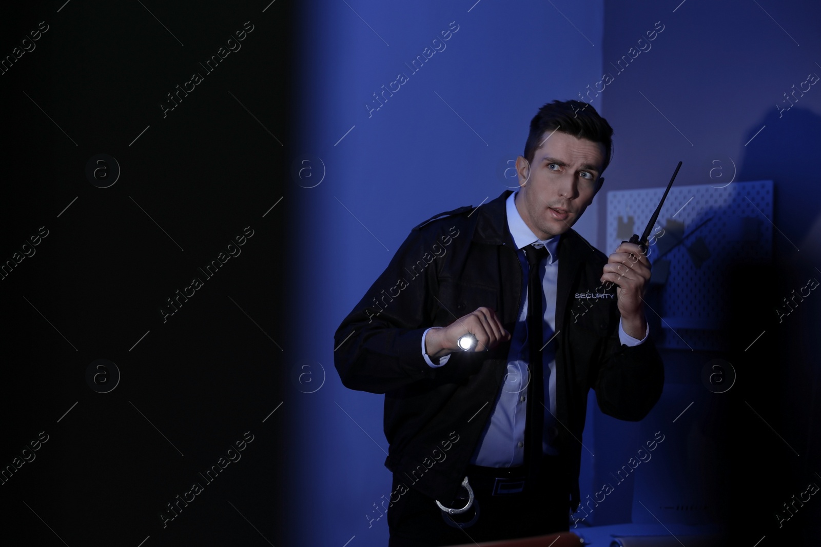 Photo of Male security guard with flashlight and portable radio transmitter in dark room