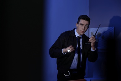 Male security guard with flashlight and portable radio transmitter in dark room