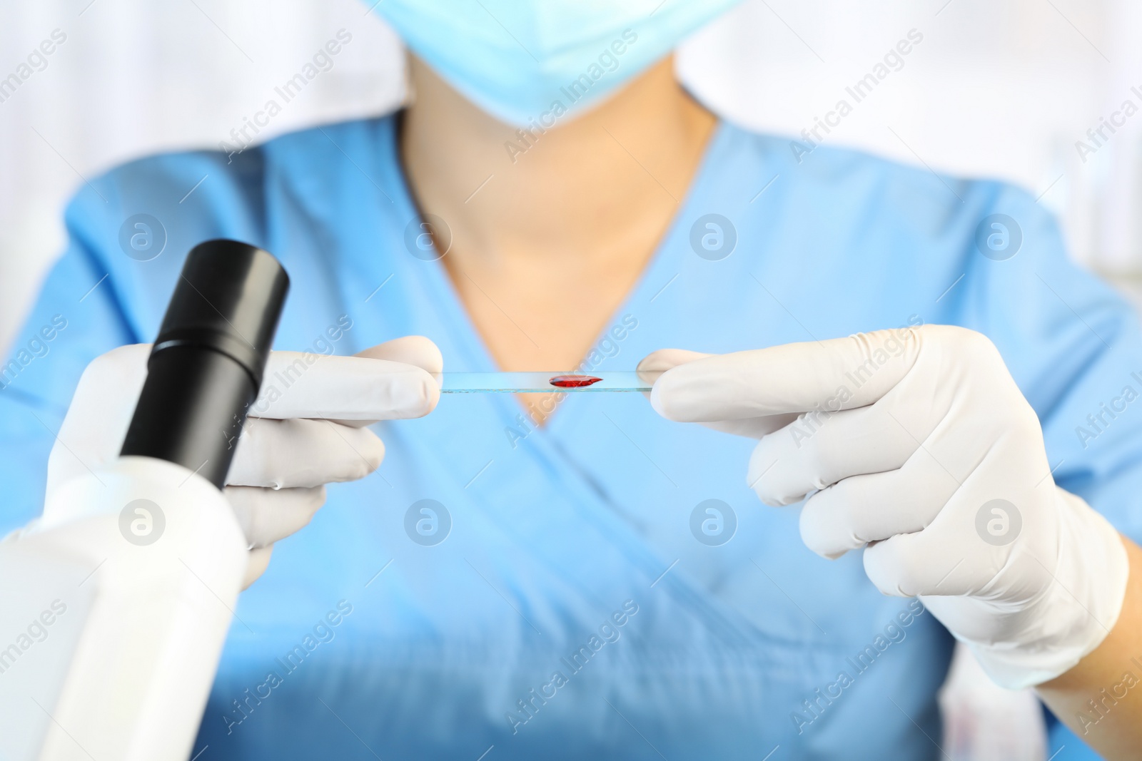 Photo of Scientist holding microscope slide with sample of red liquid in laboratory, closeup