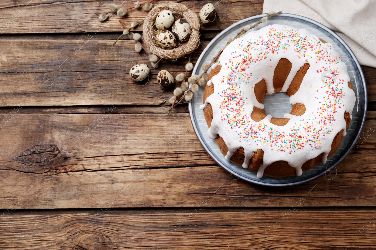 Photo of Glazed Easter cake with sprinkles and quail eggs on wooden table, flat lay. Space for text