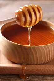 Pouring delicious honey from dipper into bowl on wooden table, closeup