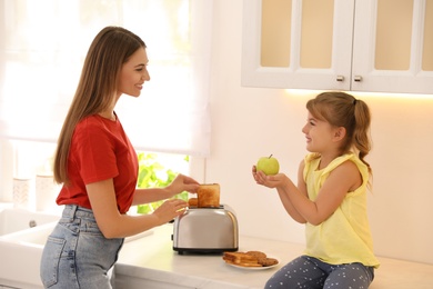 Mother and daughter preparing breakfast with toasted bread in kitchen