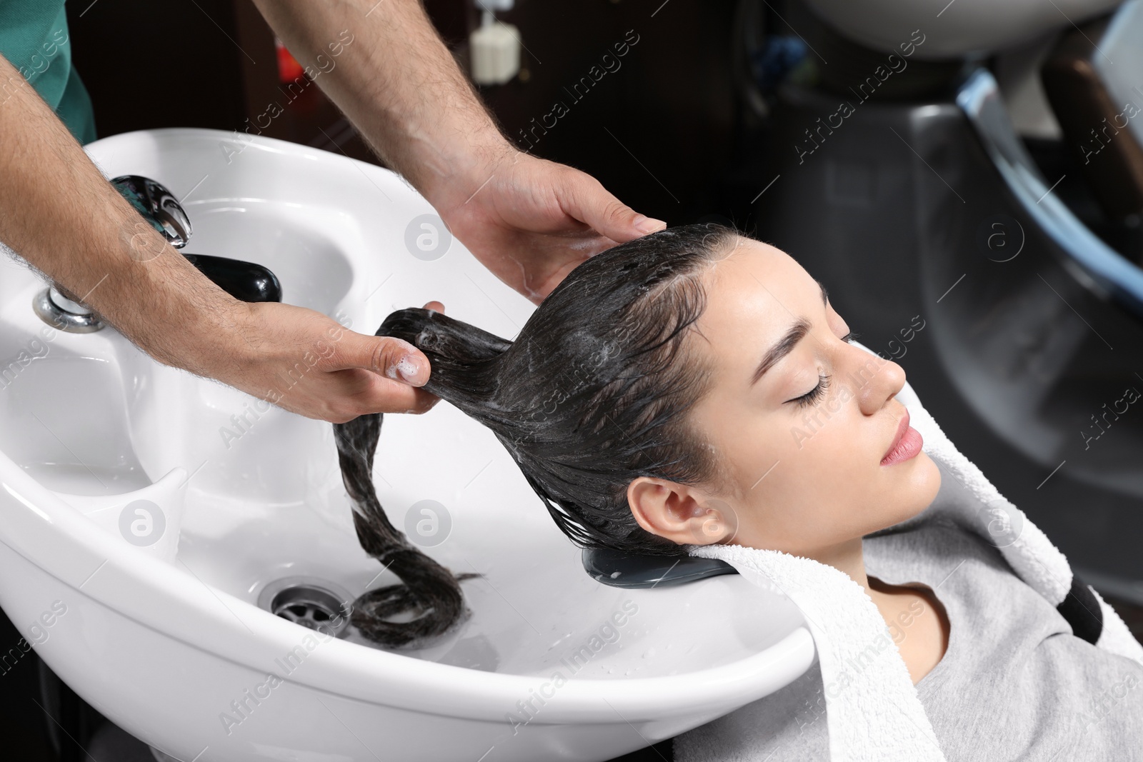 Photo of Stylist washing client's hair at sink in beauty salon